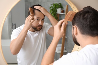 Man brushing his hair near mirror indoors. Alopecia problem