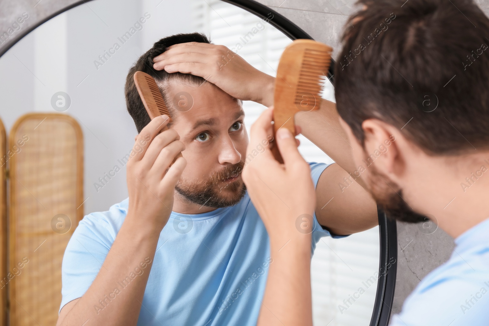 Photo of Man brushing his hair near mirror indoors. Alopecia problem