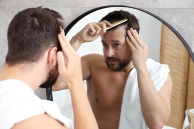 Man brushing his hair near mirror indoors. Alopecia problem