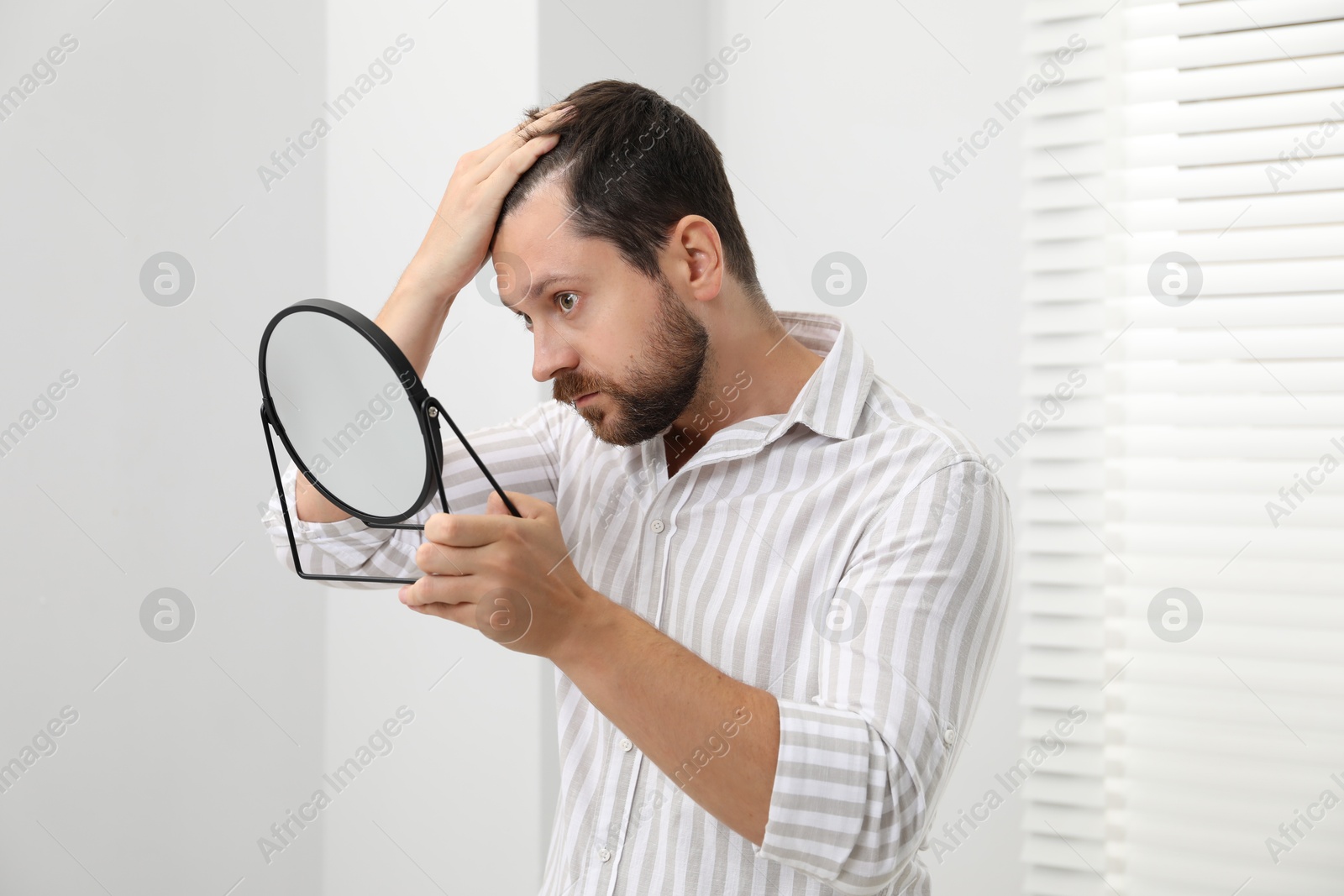 Photo of Man with hair loss problem looking at mirror indoors