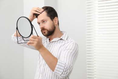 Man with hair loss problem looking at mirror indoors