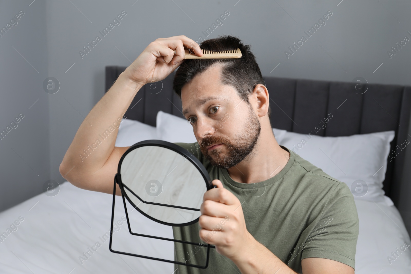 Photo of Man brushing his hair near mirror indoors. Alopecia problem