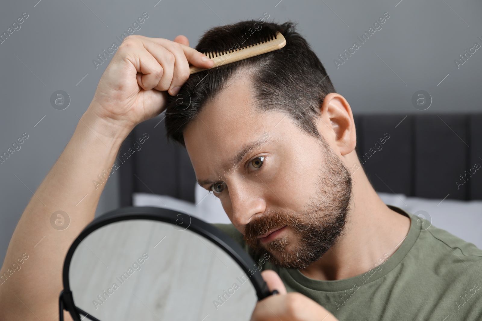 Photo of Man brushing his hair near mirror indoors. Alopecia problem