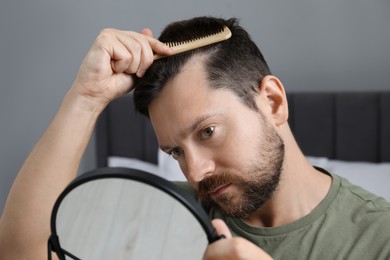 Photo of Man brushing his hair near mirror indoors. Alopecia problem