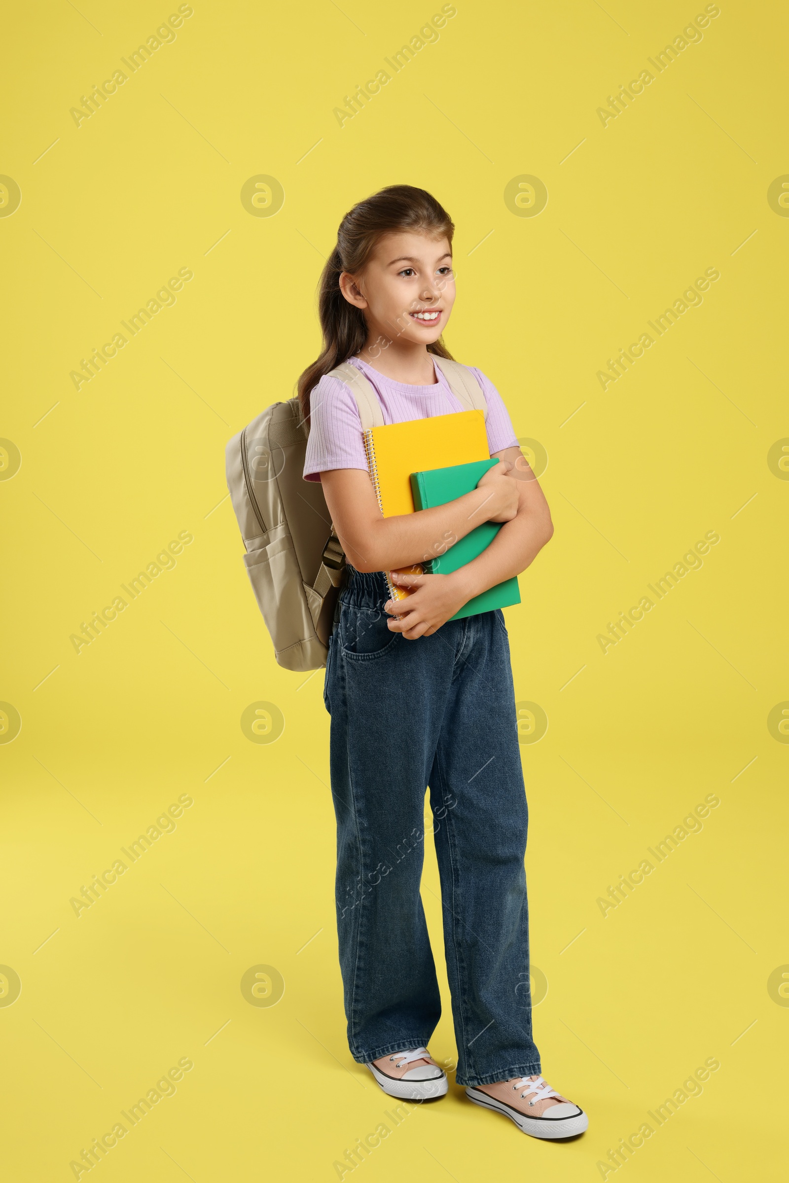 Photo of Girl with backpack and books on yellow background