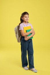 Photo of Girl with backpack and books on yellow background