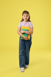 Girl with backpack and books on yellow background