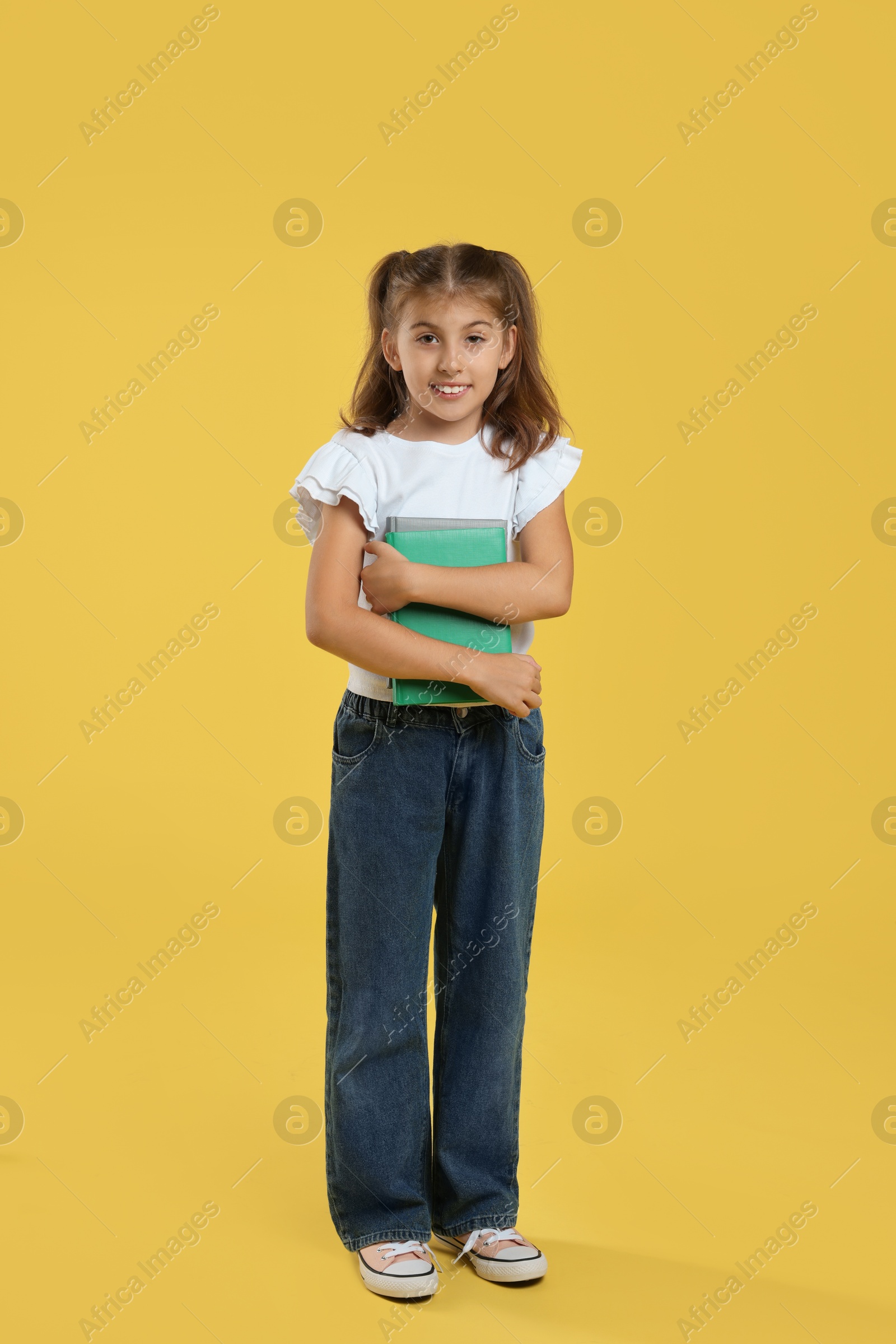 Photo of Positive girl with books on yellow background