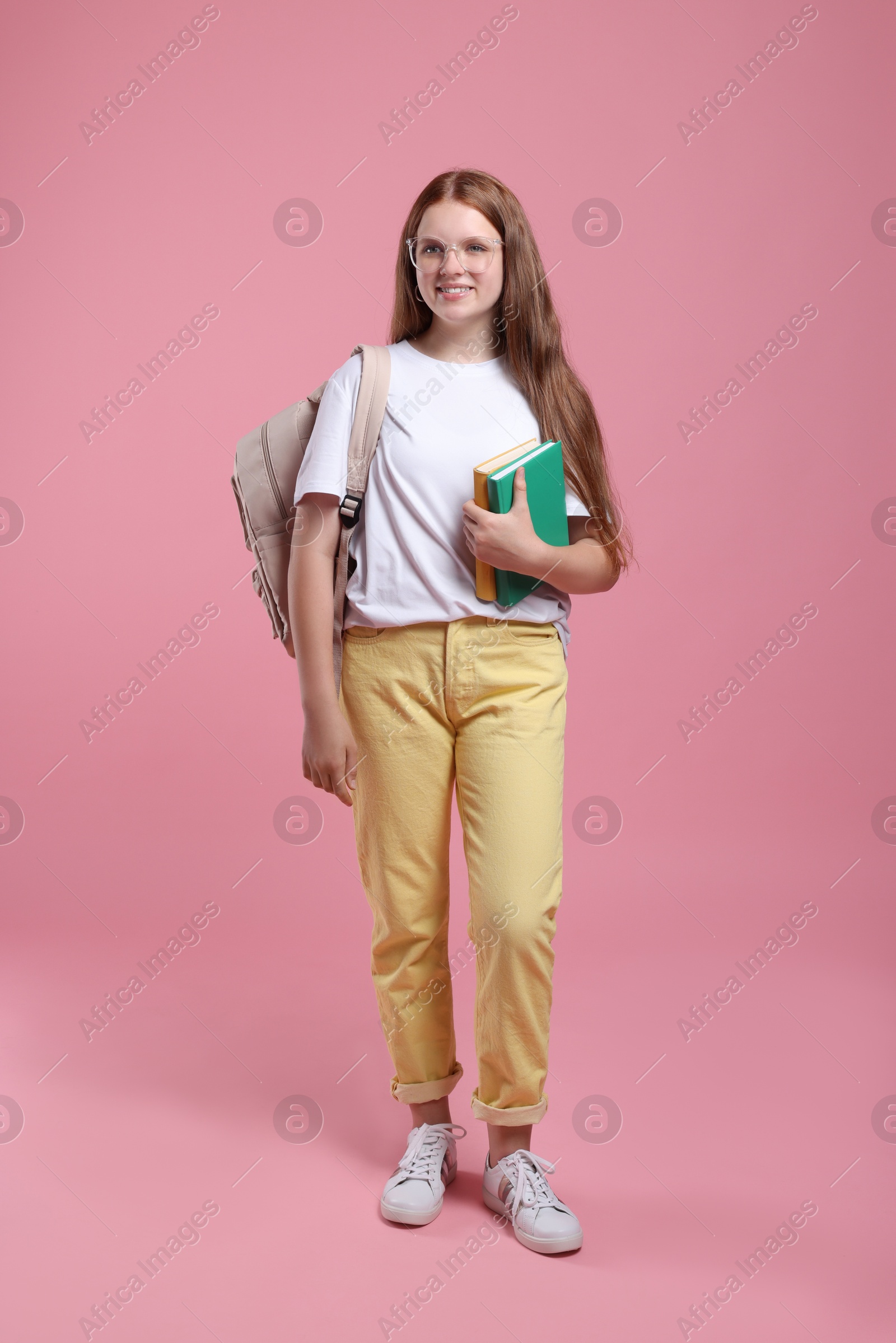 Photo of Teenage girl with backpack and books on pink background