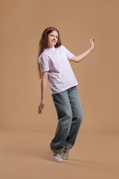 Cheerful teenage girl dancing on beige background