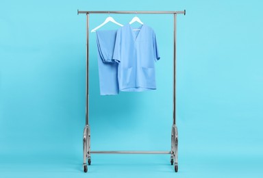 Photo of Medical worker' uniform on clothing rack against light blue background