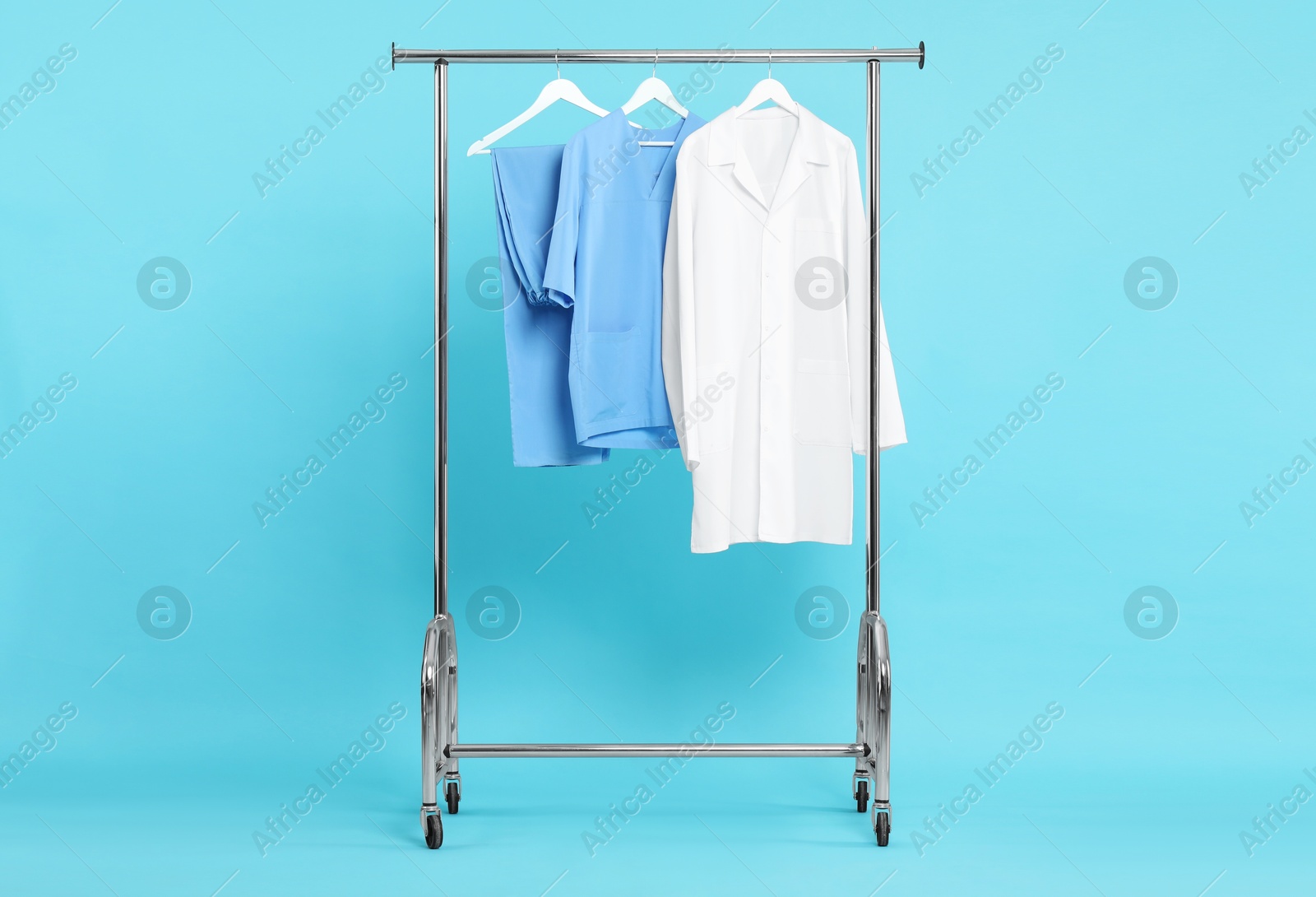 Photo of Different medical workers' uniforms on clothing rack against light blue background