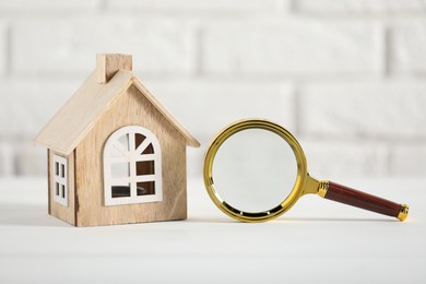 Photo of House hunting. Magnifying glass and house figure on white table