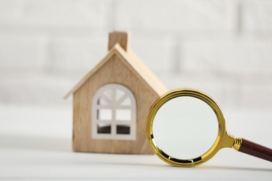 House hunting. Magnifying glass and house figure on white table, selective focus