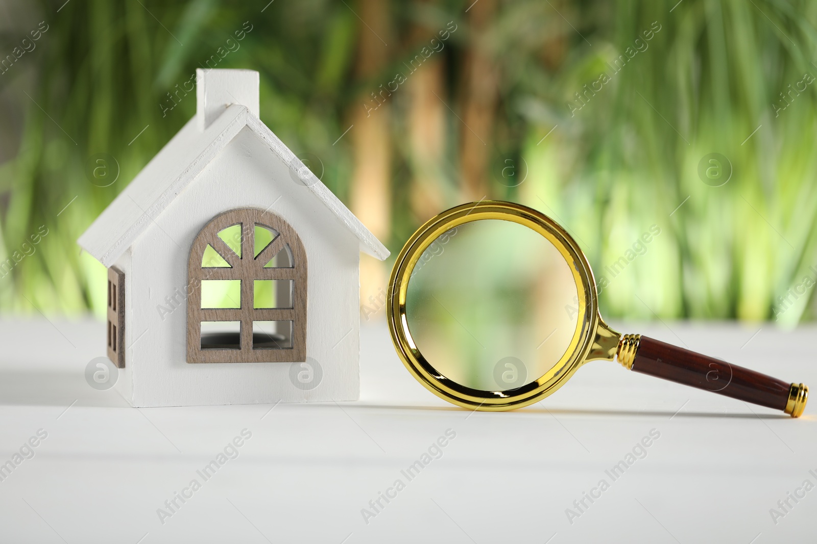 Photo of House hunting. Magnifying glass and house figure on white wooden table