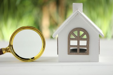 House hunting. Magnifying glass and house figure on white wooden table