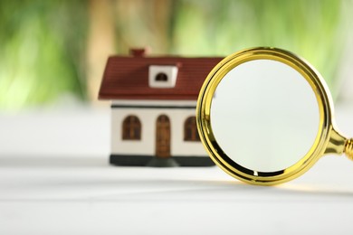 House hunting. Magnifying glass and house figure on white table