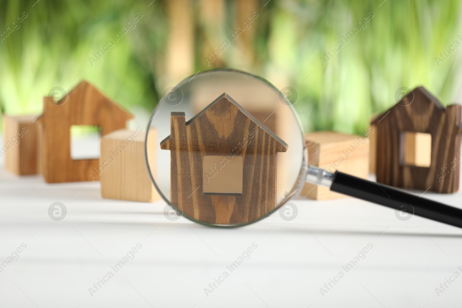 Photo of House hunting. Magnifying glass and house figure on white table