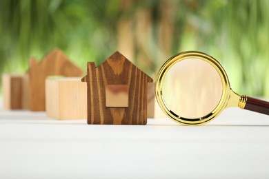 Photo of House hunting. Magnifying glass and house figure on white wooden table