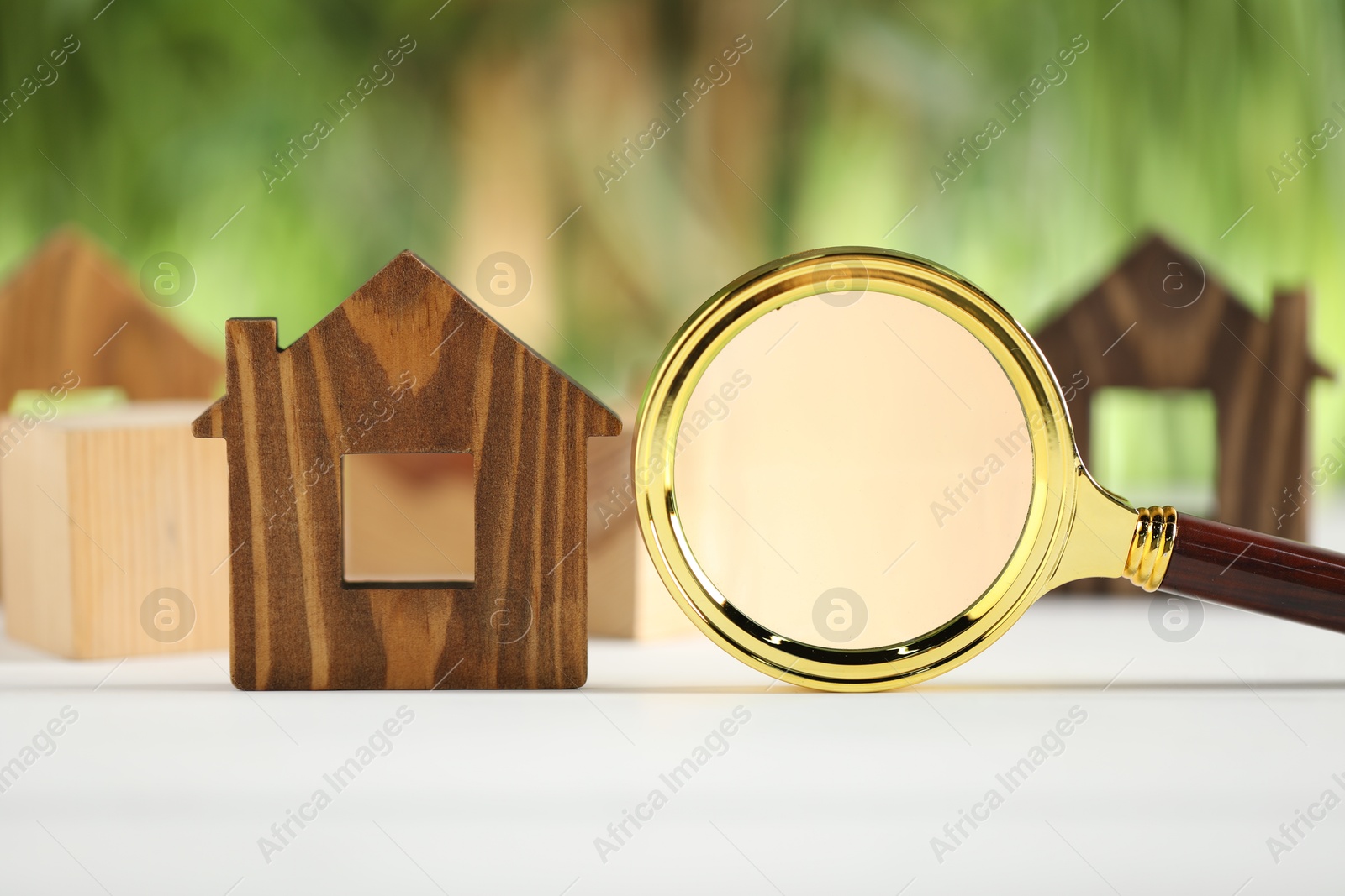 Photo of House hunting. Magnifying glass and house figure on white wooden table