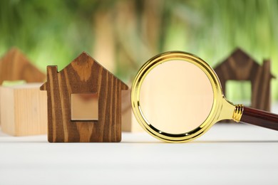 Photo of House hunting. Magnifying glass and house figure on white wooden table