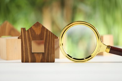 Photo of House hunting. Magnifying glass and house figure on white wooden table