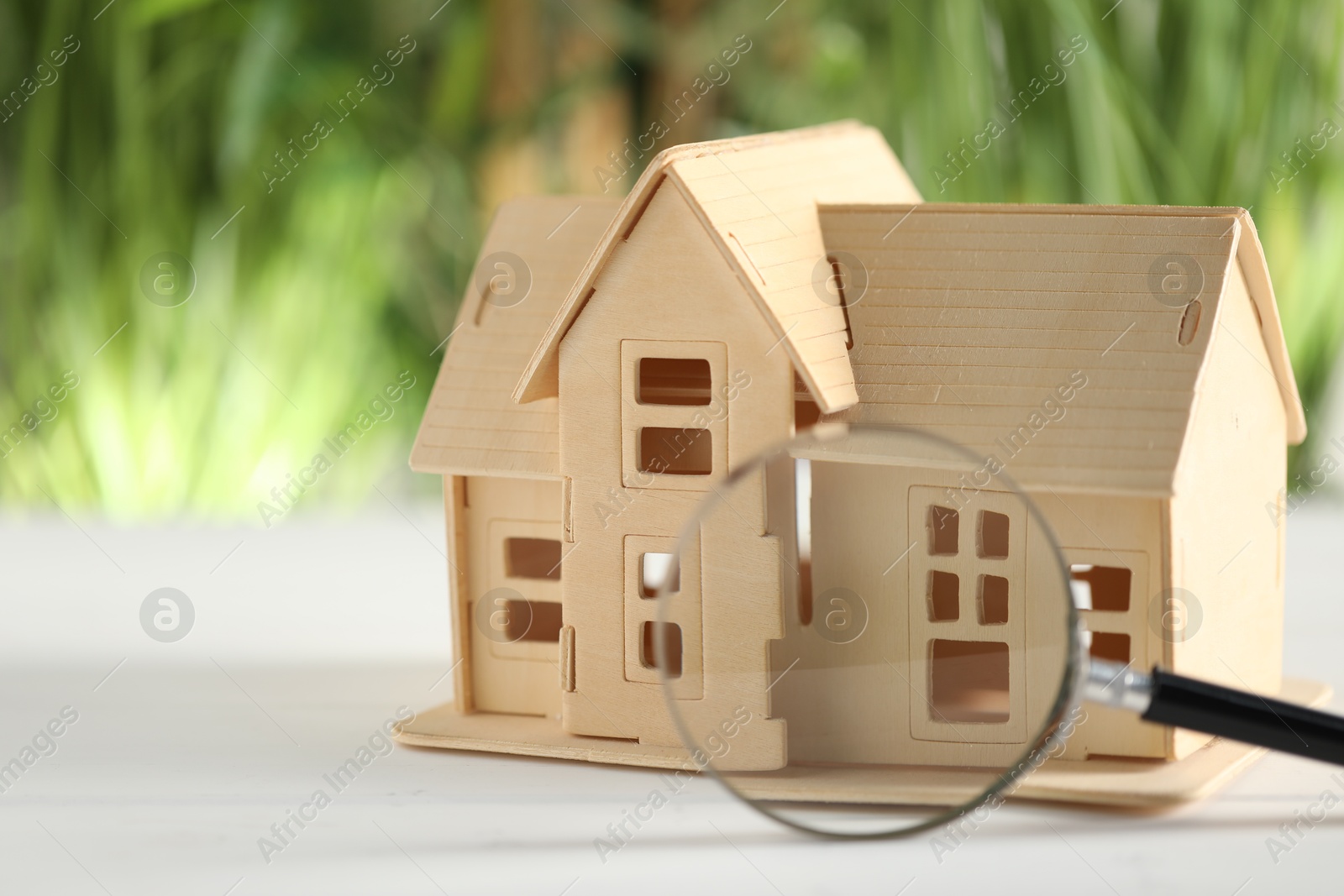 Photo of House hunting. Magnifying glass and house figure on white wooden table