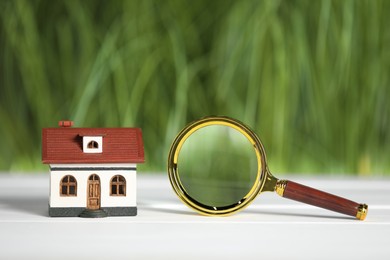 Photo of House hunting. Magnifying glass and house figure on white wooden table