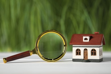 Photo of House hunting. Magnifying glass and house figure on white wooden table