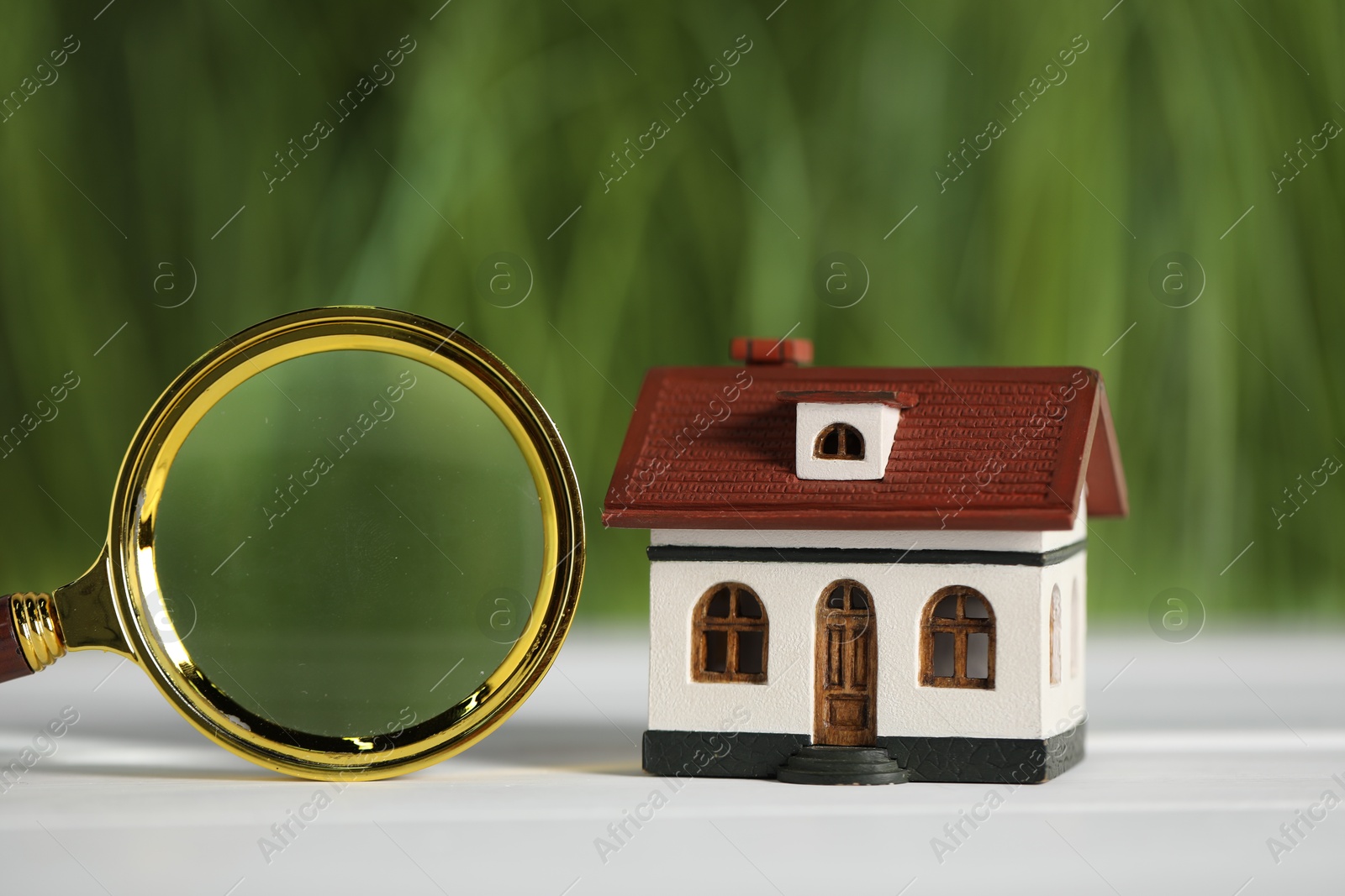 Photo of House hunting. Magnifying glass and house figure on white wooden table