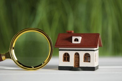 Photo of House hunting. Magnifying glass and house figure on white wooden table