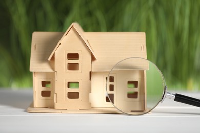 Photo of House hunting. Magnifying glass and house figure on white wooden table