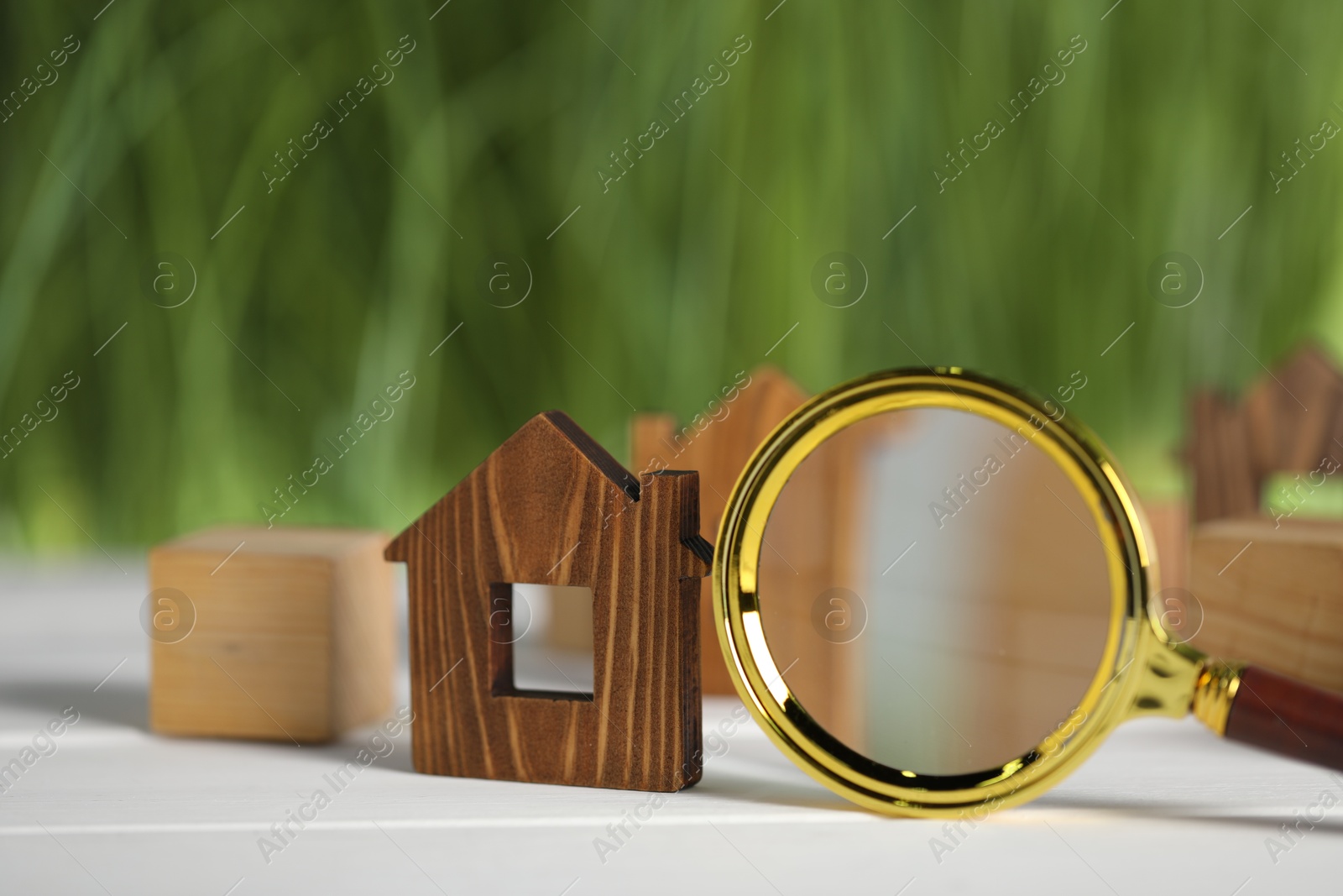 Photo of House hunting. Magnifying glass and house figure on white wooden table