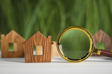 Photo of House hunting. Magnifying glass and house figure on white wooden table