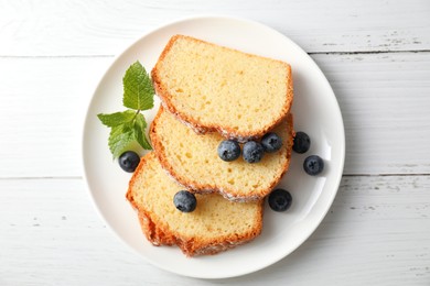 Photo of Freshly baked sponge cake, mint and blueberries on white wooden table, top view