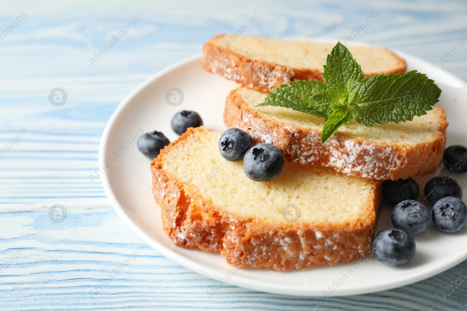 Photo of Freshly baked sponge cake, blueberries and mint on light blue wooden table, closeup