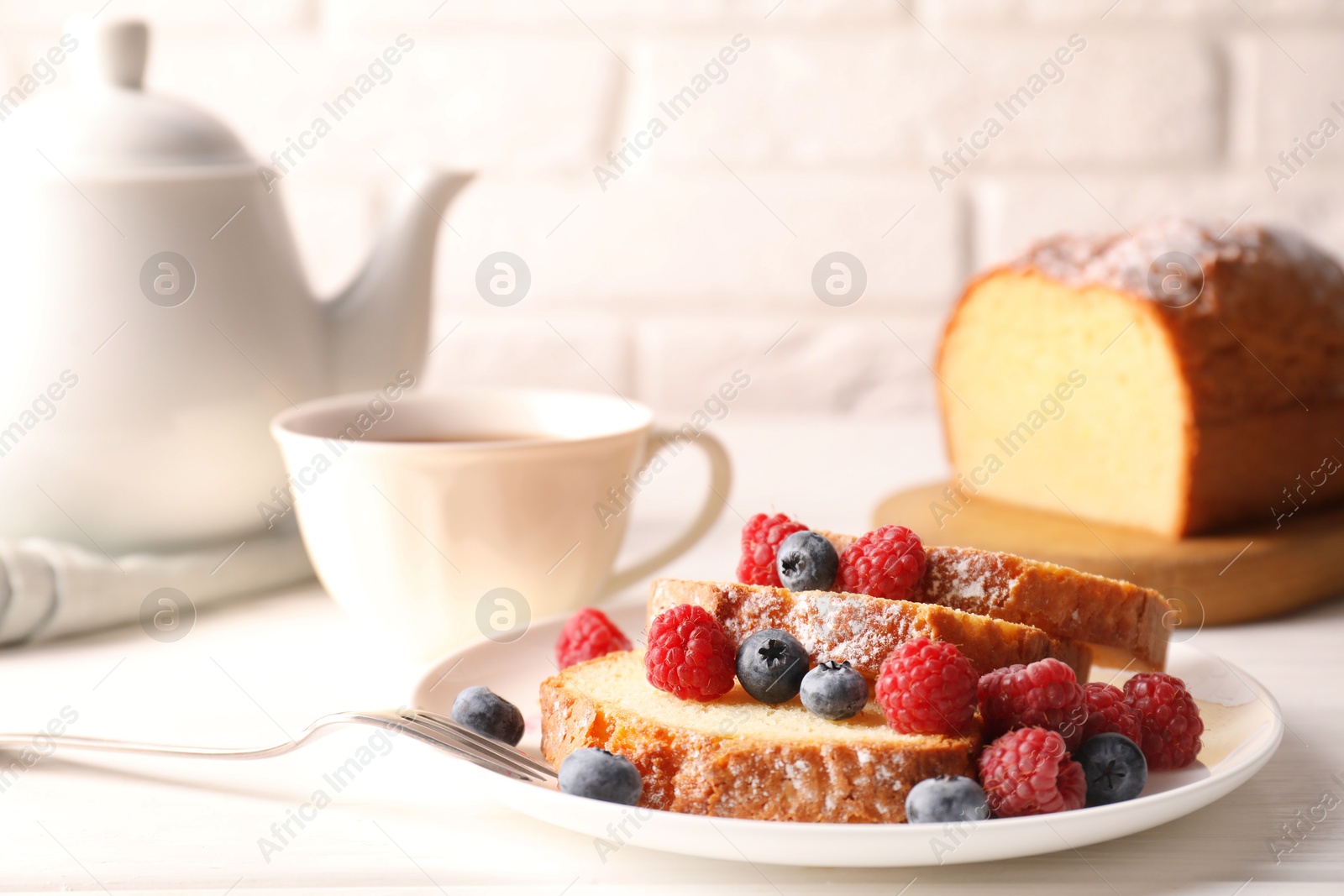 Photo of Freshly baked sponge cake, raspberries and blueberries on white wooden table