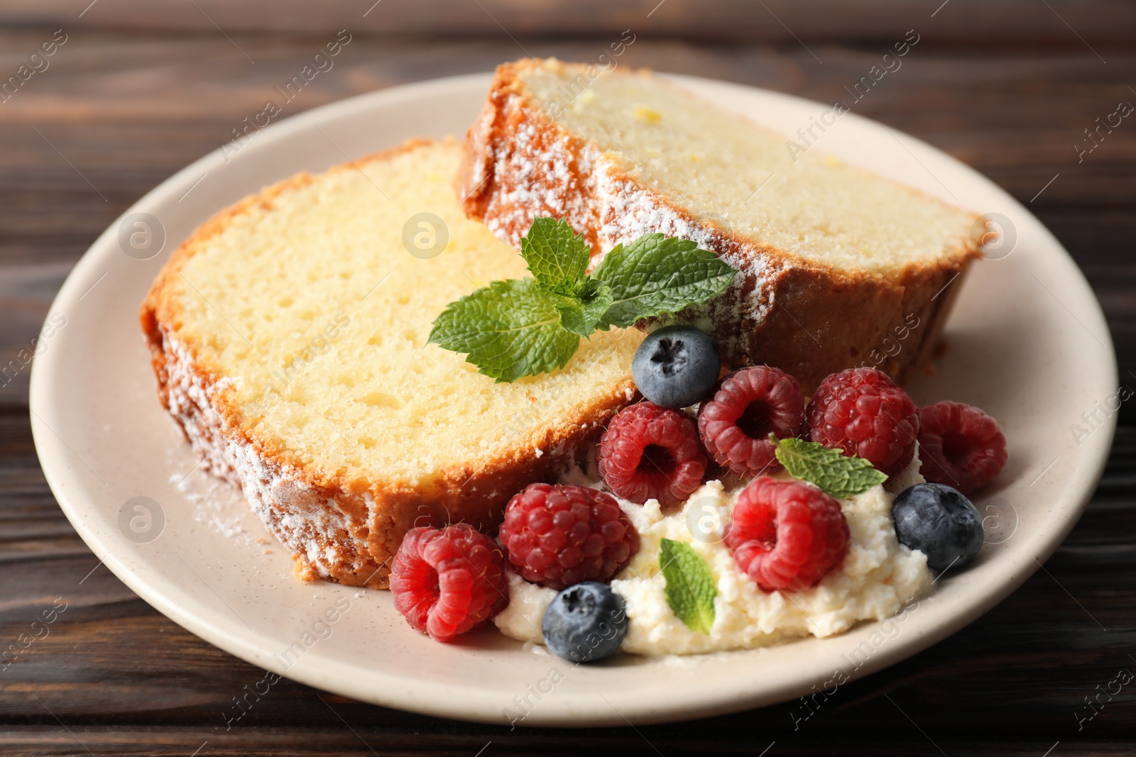 Photo of Freshly baked sponge cake, whipped cream, berries and mint on wooden table, closeup