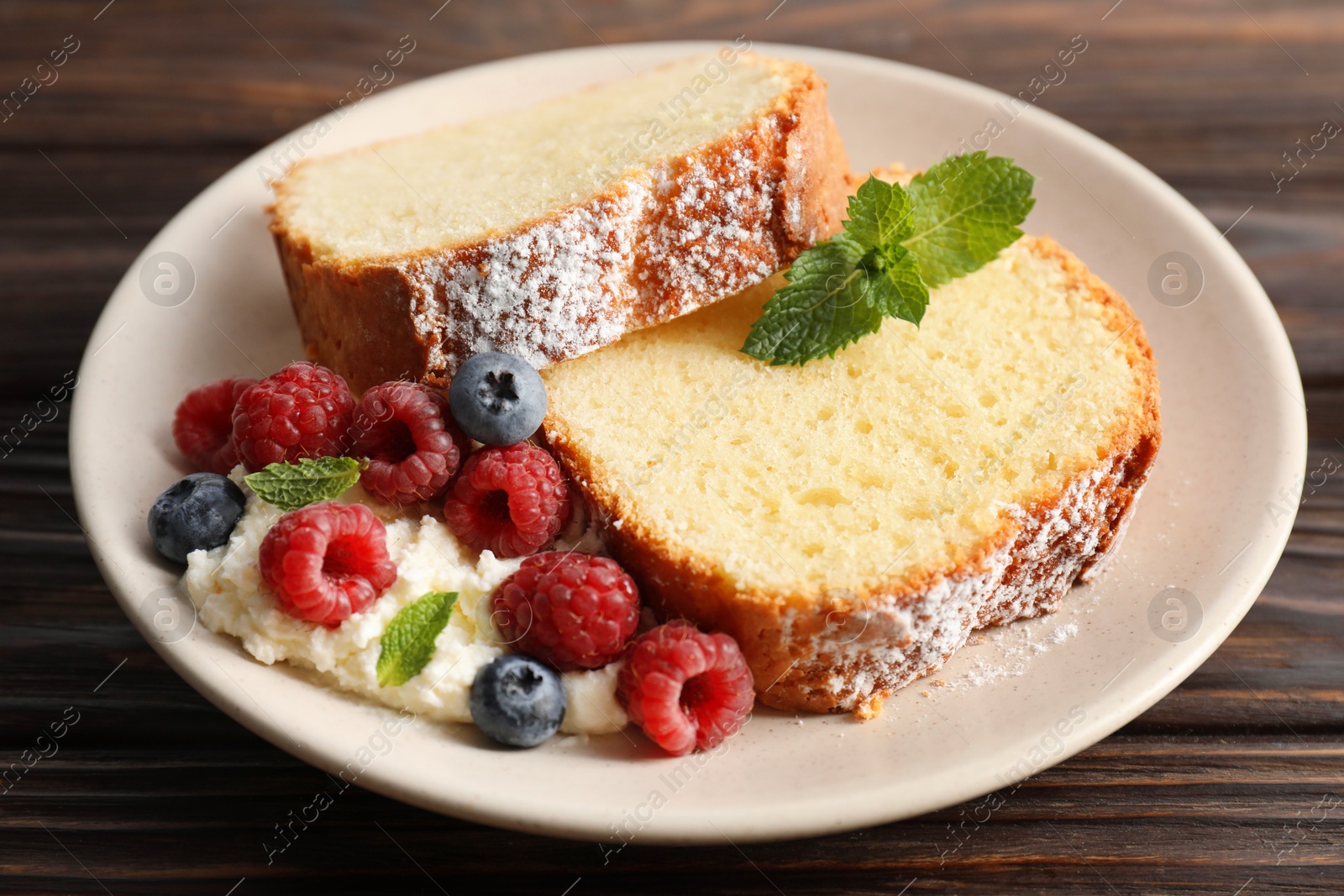 Photo of Freshly baked sponge cake, whipped cream, berries and mint on wooden table, closeup