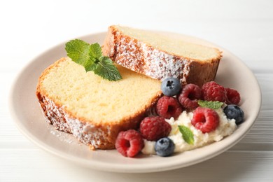 Photo of Freshly baked sponge cake, whipped cream, berries and mint on white wooden table, closeup