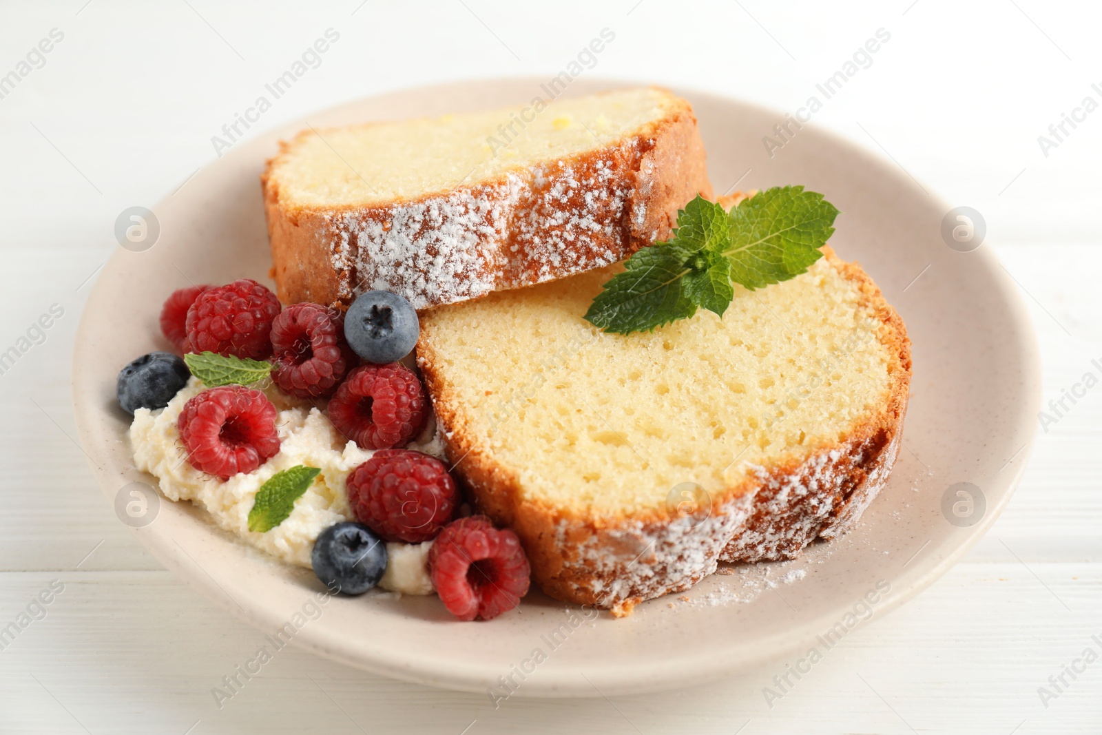 Photo of Freshly baked sponge cake, whipped cream, berries and mint on white wooden table