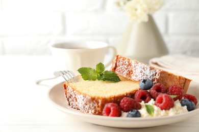 Photo of Freshly baked sponge cake, whipped cream, berries and mint on white wooden table, closeup