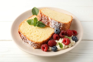 Photo of Freshly baked sponge cake, whipped cream, berries and mint on white wooden table