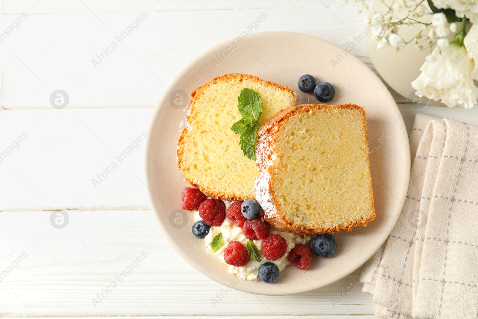 Photo of Freshly baked sponge cake, whipped cream, berries and mint on white wooden table, top view