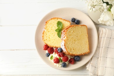 Photo of Freshly baked sponge cake, whipped cream, berries and mint on white wooden table, top view