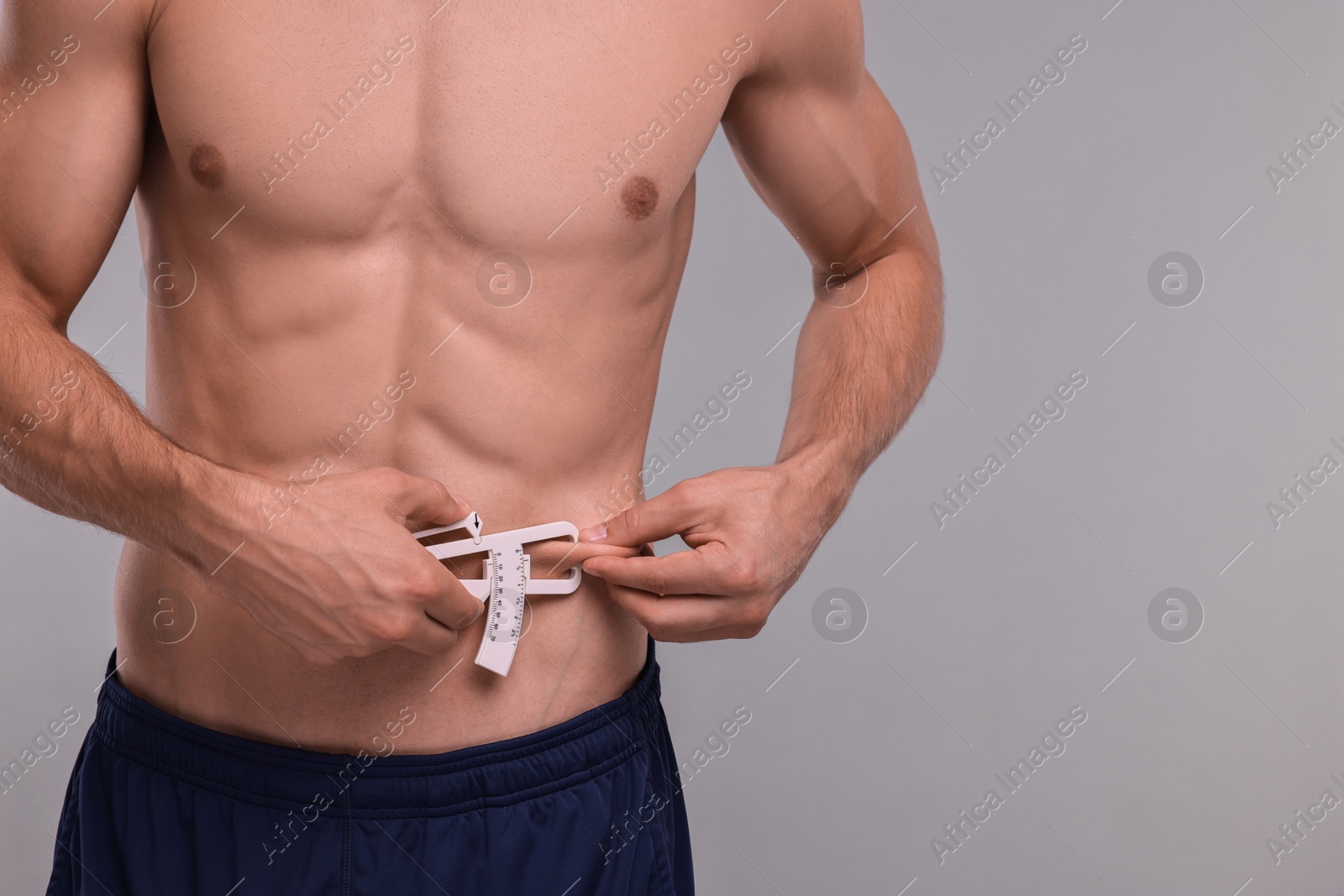 Photo of Man measuring body fat with caliper on grey background, closeup