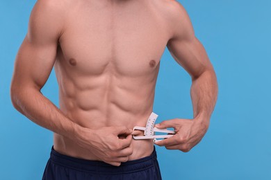 Photo of Man measuring body fat with caliper on light blue background, closeup