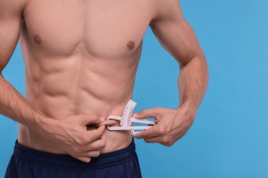 Photo of Man measuring body fat with caliper on light blue background, closeup