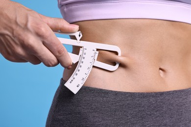 Photo of Woman measuring body fat with caliper on light blue background, closeup