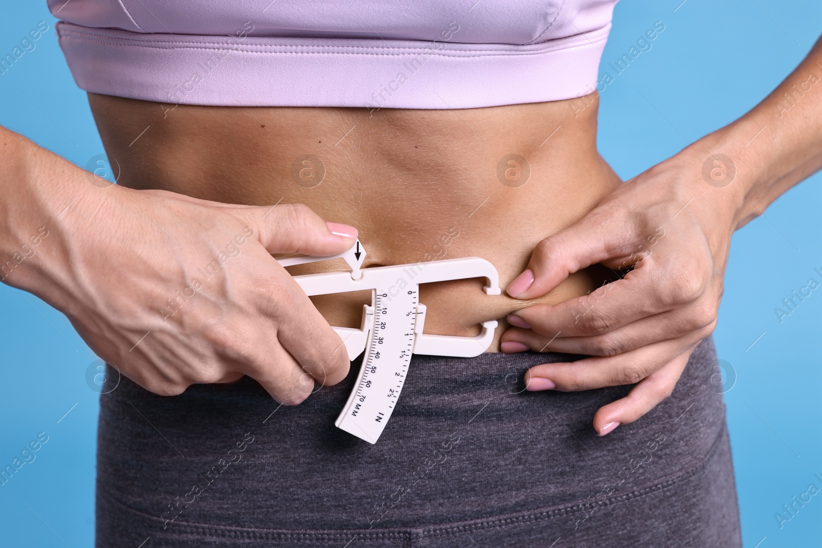 Photo of Woman measuring body fat with caliper on light blue background, closeup